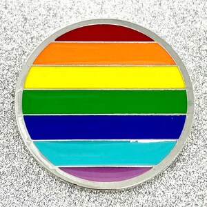 May include: A round, silver pin with a rainbow design. The pin has six stripes of red, orange, yellow, green, blue, and purple.