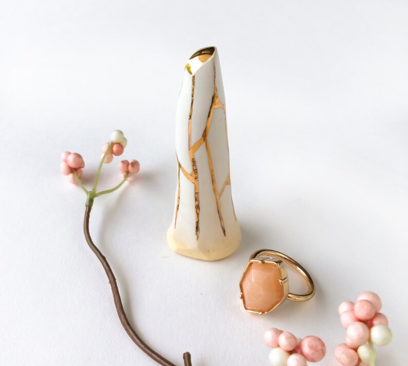 May include: A white ceramic vase with gold crackle glaze and a small, peach-coloured ring with a gold setting.