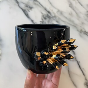 May include: Black ceramic planter with a gold crystal design. The planter is hand-painted and has a glossy finish.