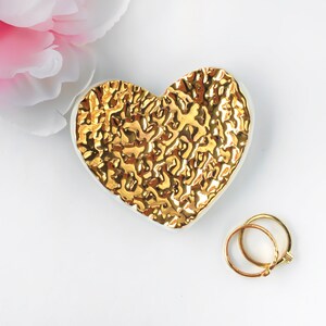 Puede incluir: Un plato de cer&aacute;mica blanca en forma de coraz&oacute;n con un dise&ntilde;o texturizado dorado. El plato es perfecto para guardar objetos peque&ntilde;os como joyas o anillos.