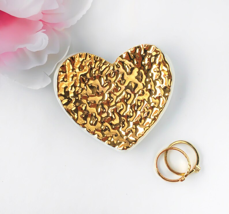 Puede incluir: Un plato de cer&aacute;mica blanca en forma de coraz&oacute;n con un dise&ntilde;o texturizado dorado. El plato es perfecto para guardar objetos peque&ntilde;os como joyas o anillos.