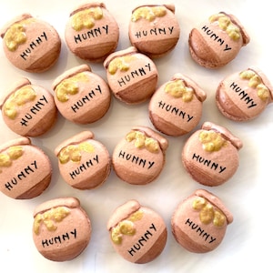 May include: A collection of 15 brown and gold macarons with the word "HUNNY" written on each one.