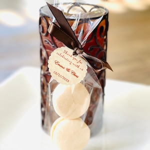 May include: Two white macarons in a clear plastic bag tied with a brown ribbon and a small tag that says "Thank you for celebrating with us. Emma & Chris 03/17/2023".