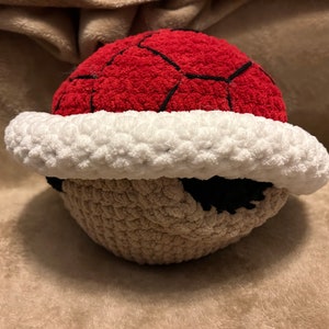 May include: A crocheted red and brown plush toy shaped like a Super Mario Bros. Koopa shell.