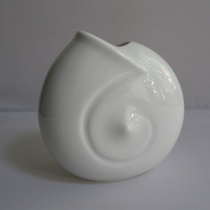 Może przedstawiać: Biały ceramiczny wazon ze spiralnym wzorem. Wazon ma kształt muszli.