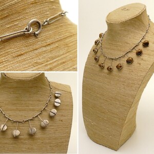 May include: A silver necklace with a chain and dangling round silver charms. The necklace is displayed on a brown mannequin.
