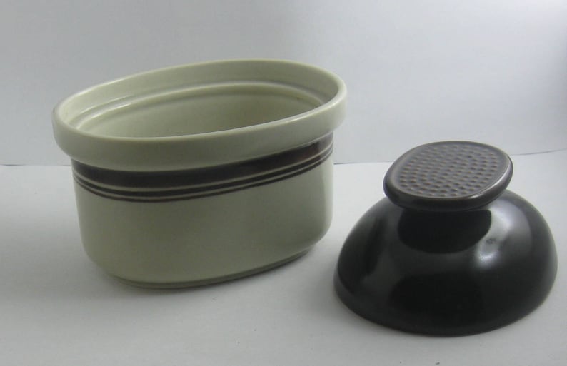 May include: A white ceramic sugar bowl with a brown stripe design and a matching black ceramic lid. The lid has a textured surface.