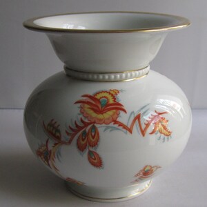 Könnte beinhalten: Weiße Porzellanvase mit rundem Korpus und ausgestelltem oberen Rand. Die Vase hat einen goldenen Rand und ein florales Design in Orange-, Rot- und Gelbtönen.