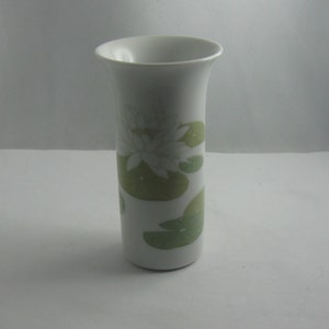 Puede incluir: Jarrón de cerámica blanco con un diseño floral verde y blanco. El jarrón es cilíndrico y tiene una parte superior ligeramente acampanada.