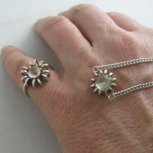 May include: A silver ring and necklace with a clear crystal in the centre of each piece. Both pieces have a sunburst design.