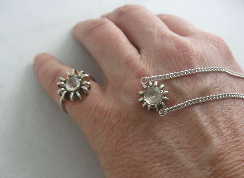 May include: A silver ring and necklace with a clear crystal in the centre of each piece. Both pieces have a sunburst design.
