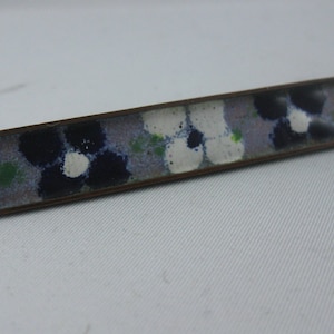 May include: A long, rectangular, bronze-colored bar pin with a floral design. The design features white, blue, and green flowers on a light purple background.