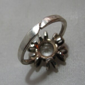 May include: Silver ring with a clear stone setting surrounded by smaller stones.