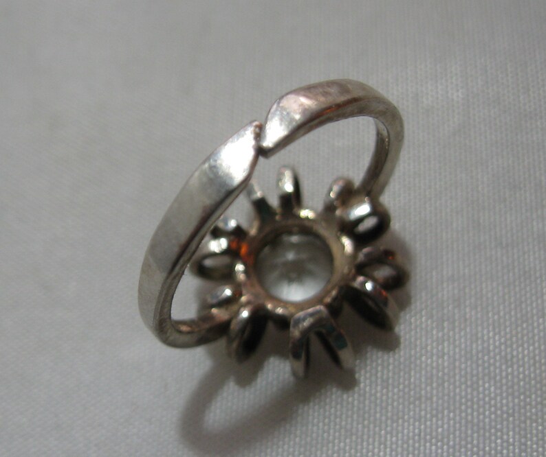 May include: Silver ring with a clear stone setting surrounded by smaller stones.