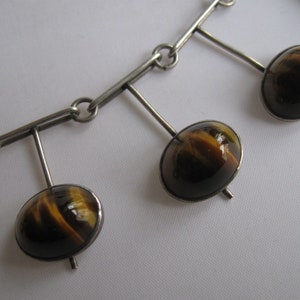 May include: A silver necklace with a chain and four dangling pendants. Each pendant features a round, brown and gold tiger's eye stone.