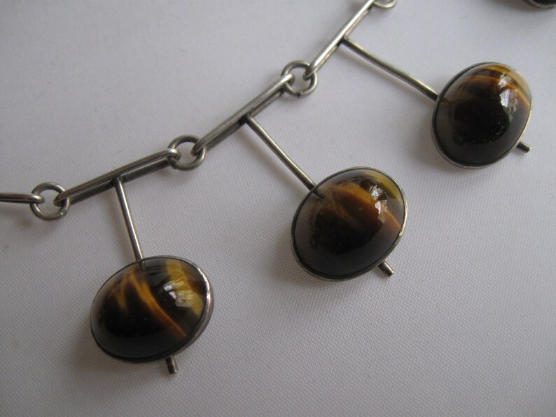 May include: A silver necklace with a chain and four dangling pendants. Each pendant features a round, brown and gold tiger's eye stone.