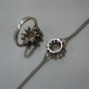 May include: A silver ring and bracelet set featuring a clear stone surrounded by smaller stones. Both the ring and bracelet are shaped like a flower.
