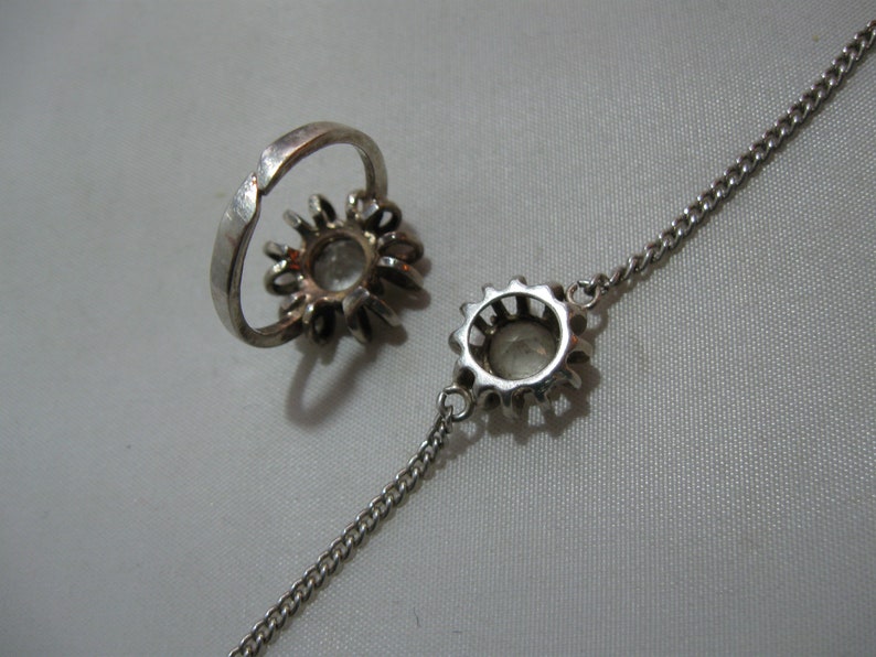 May include: A silver ring and bracelet set featuring a clear stone surrounded by smaller stones. Both the ring and bracelet are shaped like a flower.