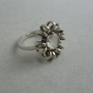 May include: A silver ring featuring a clear crystal stone set in a flower-shaped design.