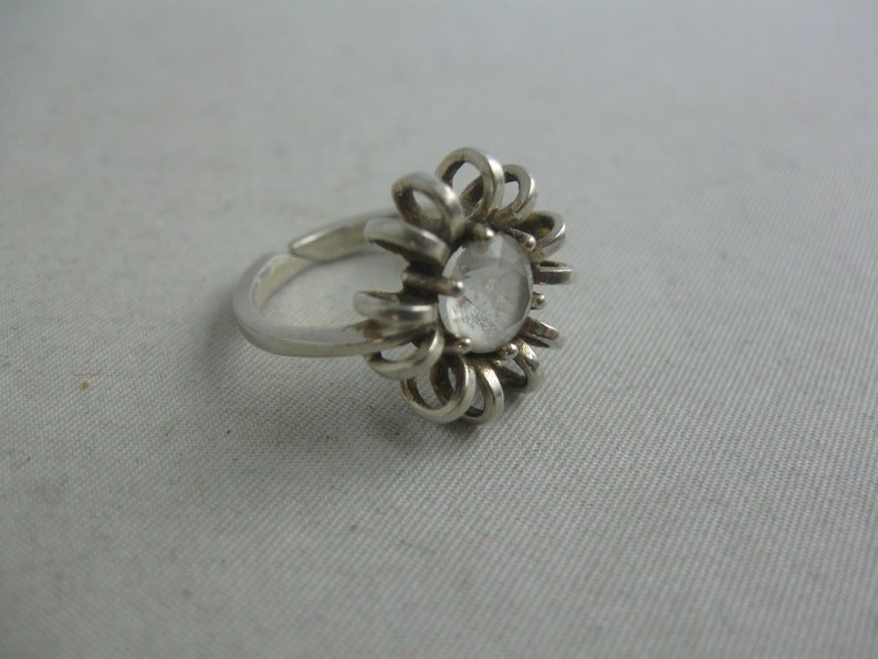 May include: A silver ring featuring a clear crystal stone set in a flower-shaped design.