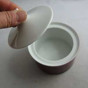 May include: A white ceramic lidded dish with a purple base. The lid is slightly domed and has a smooth, glossy finish.