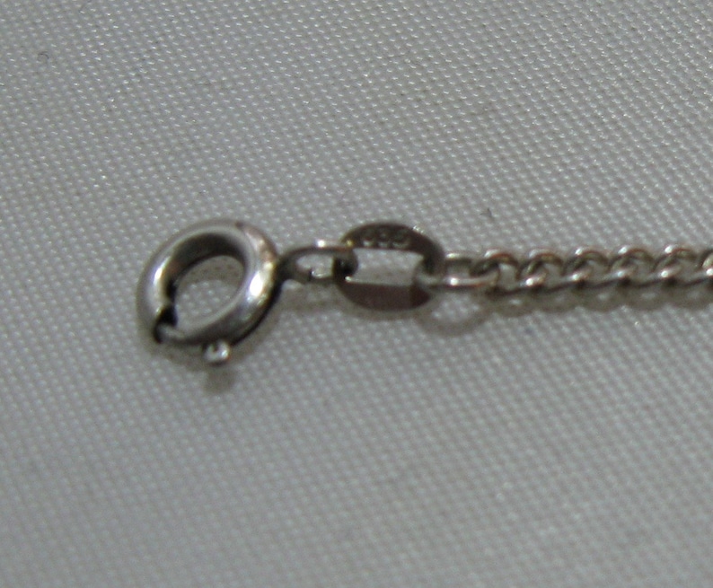 May include: Close-up of a silver chain necklace clasp with a lobster claw closure. The chain is a curb style with a polished finish.