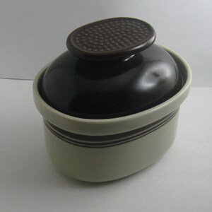 May include: A brown and white ceramic crock with a brown lid. The lid has a textured pattern.