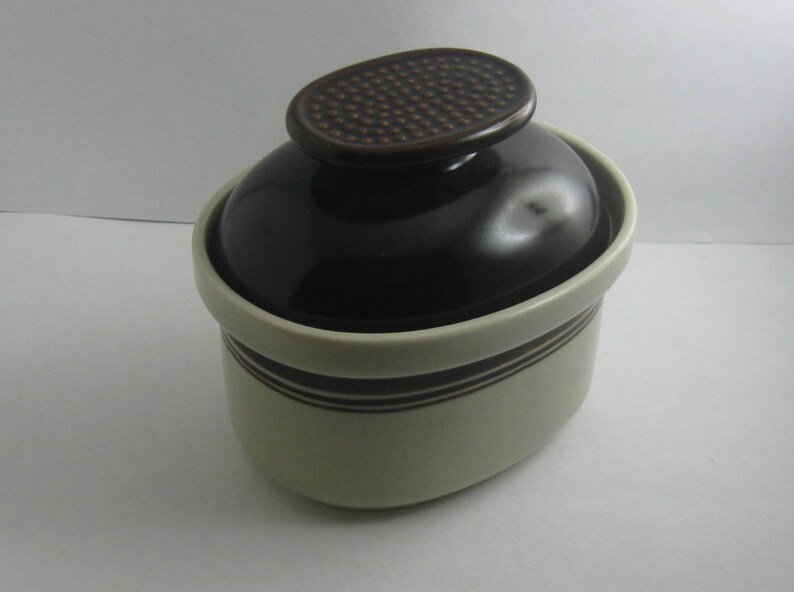 May include: A brown and white ceramic crock with a brown lid. The lid has a textured pattern.