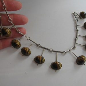 May include: A silver chain necklace with a dangling design featuring tiger's eye stones. The stones are a mix of brown and gold.