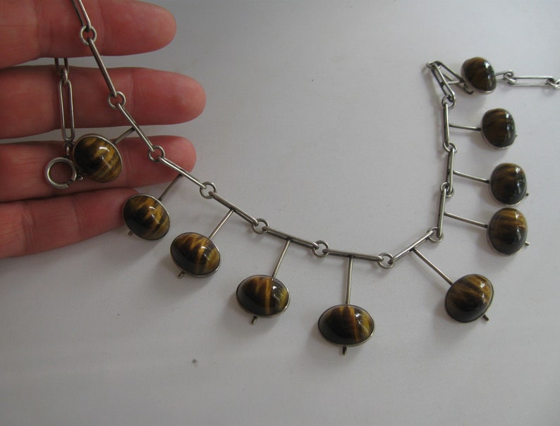 May include: A silver chain necklace with a dangling design featuring tiger's eye stones. The stones are a mix of brown and gold.