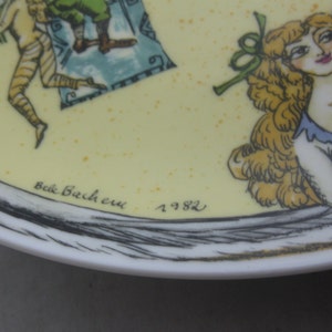 May include: A decorative plate with a yellow background and a detailed illustration. The artwork features figures in a classical style, with a woman with blonde hair and a man with a beard. The plate is signed "Belle Bachere" and dated "1982".
