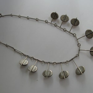 May include: A silver necklace with a chain and multiple oval-shaped pendants hanging from it.