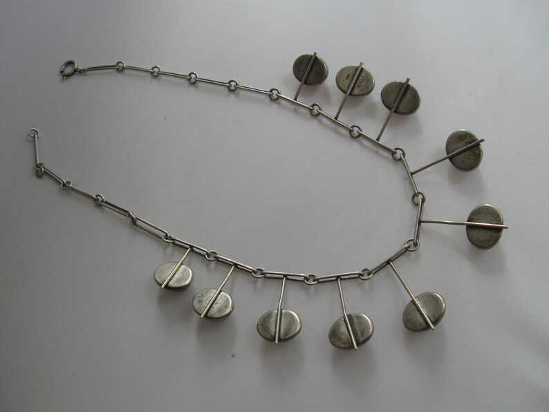 May include: A silver necklace with a chain and multiple oval-shaped pendants hanging from it.