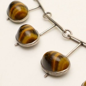 May include: A silver necklace with a chain and five tiger's eye stones. The stones are brown and gold with a striated pattern.