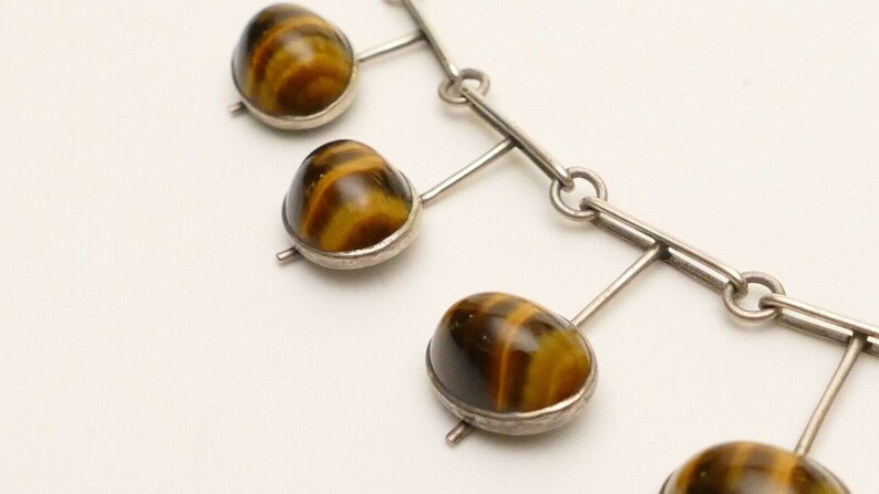 May include: A silver necklace with a chain and five tiger's eye stones. The stones are brown and gold with a striated pattern.