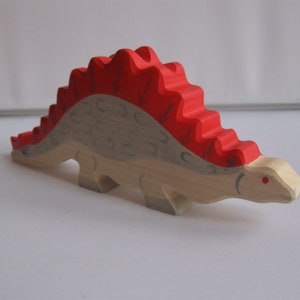 Könnte beinhalten: Ein hölzerner Spielzeug-Dinosaurier mit einem roten, stacheligen Rücken und einem hellbraunen Körper. Der Dinosaurier hat ein kleines rotes Auge.