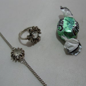 May include: A silver ring and bracelet with clear stones, and a green and silver wrapped sweet with the word "Mint" on it.