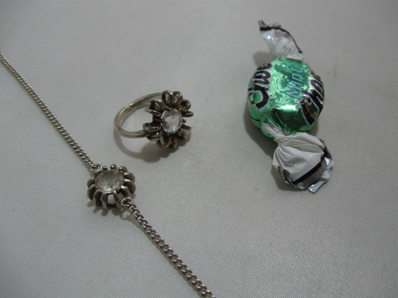 May include: A silver ring and bracelet with clear stones, and a green and silver wrapped sweet with the word "Mint" on it.