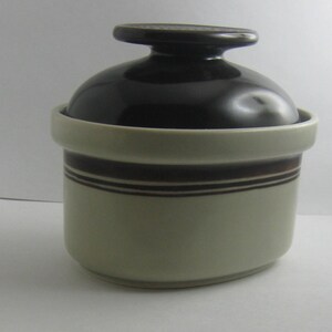 May include: A brown and white ceramic jar with a lid. The jar has a brown stripe around the middle and a brown rim.