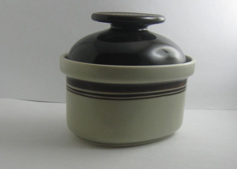 May include: A brown and white ceramic jar with a lid. The jar has a brown stripe around the middle and a brown rim.