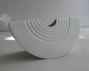 Può includere: Vaso in ceramica bianca con un design unico e curvo. Il vaso presenta una serie di cerchi concentrici che creano un effetto ondulato.