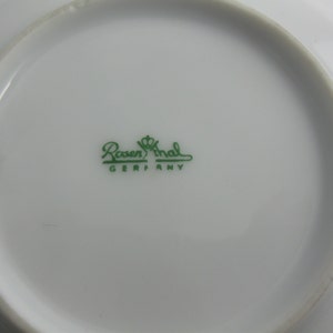 May include: Close-up of the bottom of a white saucer with a green logo that reads "Rosenthal Germany".