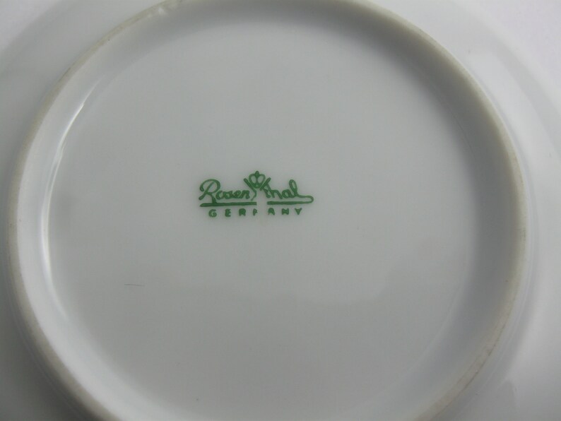 May include: Close-up of the bottom of a white saucer with a green logo that reads "Rosenthal Germany".