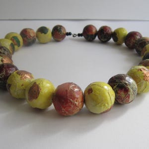 May include: A necklace made of round, yellow, brown, and red beads. The beads are made of paper and have a textured surface.