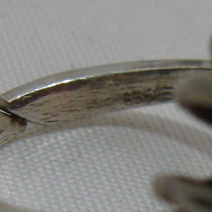 May include: Close-up of a silver ring with a textured band. The inside of the band is marked with the number "925", indicating that the ring is made of sterling silver.