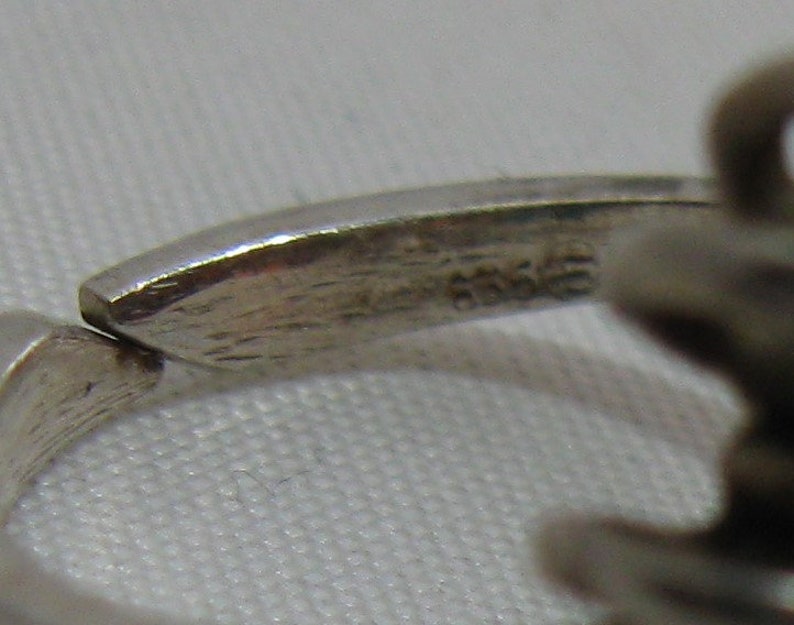 May include: Close-up of a silver ring with a textured band. The inside of the band is marked with the number "925", indicating that the ring is made of sterling silver.