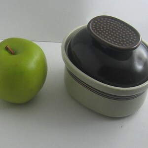 May include: A white and brown ceramic dish with a lid. The lid has a brown, textured design. The dish is oval shaped and has a brown rim.