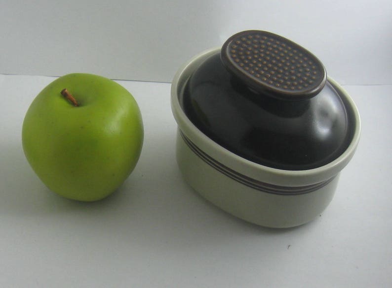 May include: A white and brown ceramic dish with a lid. The lid has a brown, textured design. The dish is oval shaped and has a brown rim.