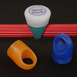 May include: Three bottle caps, one white with blue lettering that says "Pfand-flasche", one orange, and one blue.