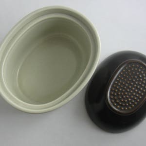 May include: A set of two oval ceramic dishes. One dish is light green with a smooth finish. The other dish is black with a brown oval design.